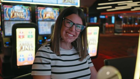 Foto de Una joven hispana sonriente disfrutando de su tiempo en un vibrante casino que refleja su energía ganadora. - Imagen libre de derechos