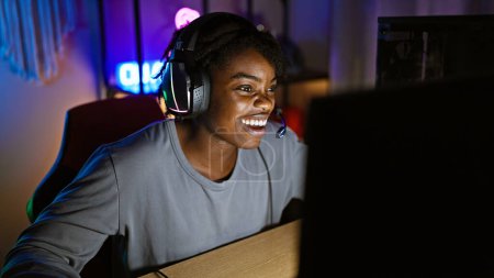 Téléchargez les photos : Une jeune femme aux dreadlocks souriant et portant un casque dans une salle de jeux éclairée au néon la nuit - en image libre de droit