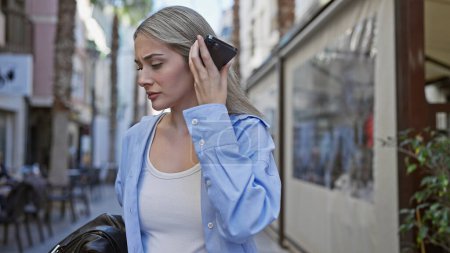 Eine schöne junge kaukasische Frau lauscht aufmerksam einer Voicemail auf ihrem Smartphone, während sie auf einer städtischen Straße steht.