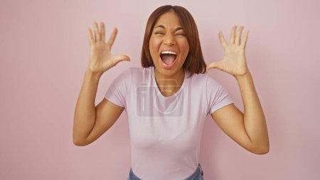 Foto de Mujer afroamericana riendo alegremente con las manos en alto sobre un fondo rosado, retratando positividad y felicidad. - Imagen libre de derechos