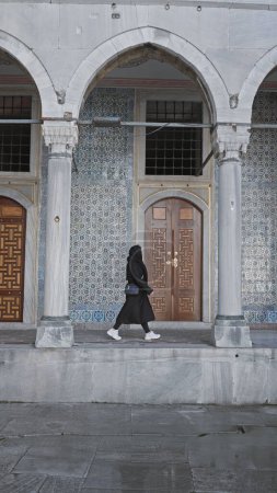 Téléchargez les photos : Une femme se promène par l'architecture ornée et les tuiles du palais topkapi d'Istanbul, incarnant l'exploration culturelle - en image libre de droit