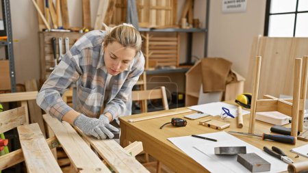 Téléchargez les photos : Jeune femme ponçant du bois dans un atelier de menuiserie bien équipé, mettant en valeur l'artisanat et la précision. - en image libre de droit