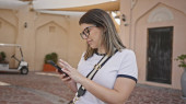 A young hispanic woman uses her smartphone on a traditional arabic street in doha, showcasing urban life. Stickers #710171058