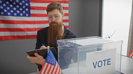 Un barbudo con gafas tomando notas junto a una urna en un centro electoral con la bandera americana