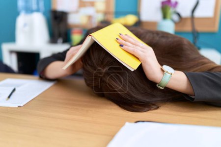 Téléchargez les photos : Jeune belle travailleuse d'affaires stressée couvrant la tête avec le livre au bureau - en image libre de droit