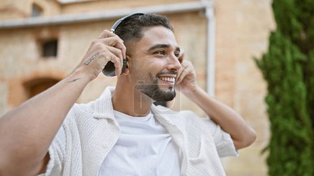 Photo for A smiling bearded man enjoying music with headphones in an urban outdoor setting. - Royalty Free Image