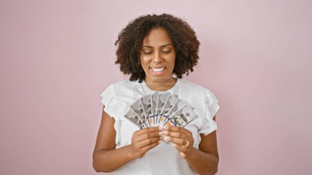 Téléchargez les photos : Femme afro-américaine souriante, tenant des dollars américains, fond rose - en image libre de droit