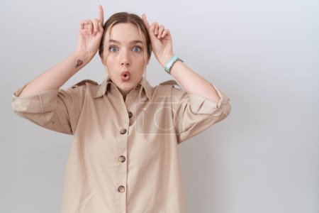 Téléchargez les photos : Jeune femme caucasienne portant une chemise décontractée faisant un geste drôle avec le doigt sur la tête comme des cornes de taureau - en image libre de droit