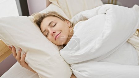 Téléchargez les photos : Une jeune femme blonde sereine qui dort paisiblement dans une chambre lumineuse, incarnant détente et confort. - en image libre de droit