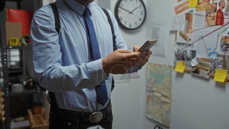 Handsome hispanic man using smartphone in police station with evidence board behind
