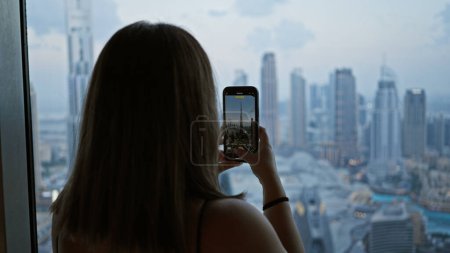 Foto de Mujer capturando el horizonte de Dubái en un teléfono inteligente desde el observatorio, que representa viajes, paisajes urbanos y fotografía - Imagen libre de derechos