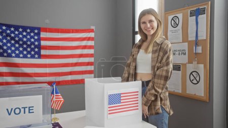 Una joven rubia sonríe en un ambiente de colegio electoral de EE.UU. con cabinas de votación, banderas americanas y carteles informativos.