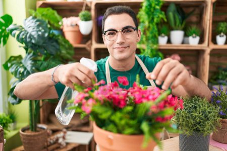 Téléchargez les photos : Young hispanic man florist using diffuser watering plant at flower shop - en image libre de droit