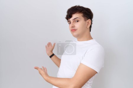 Foto de Joven hombre no binario con camiseta blanca casual invitando a entrar sonriente natural con la mano abierta - Imagen libre de derechos