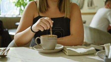 Photo for A woman stirs coffee at a restaurant table, depicting a casual dining scene. - Royalty Free Image