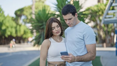 Téléchargez les photos : Beau couple utilisant smartphone debout ensemble au parc - en image libre de droit