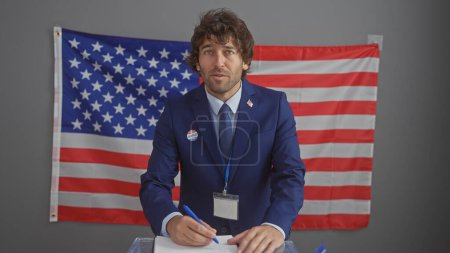 Handsome hispanic man with a beard in a blue suit voting at an american electoral college with a us flag background.