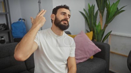 Un hombre barbudo de mediana edad hace gestos de un arma en su cabeza en una sala de estar, expresando frustración o desesperación.