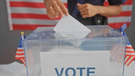 Hombre afroamericano votando en un proceso electoral de estados unidos con una papeleta y bandera en el fondo.
