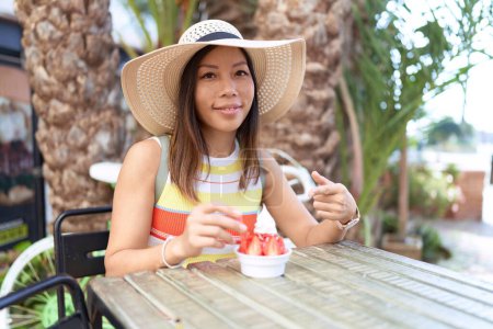Téléchargez les photos : Femme chinoise du Moyen Âge mangeant de la crème glacée à l'extérieur sur une terrasse souriant heureux pointant avec la main et le doigt - en image libre de droit