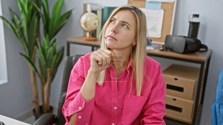 Femme blonde pensive en chemise rose contemplant dans un cadre de bureau moderne