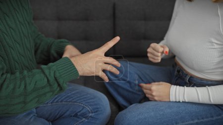 A couple seated indoors having a discussion in a living room, with gestures indicating a conversation.