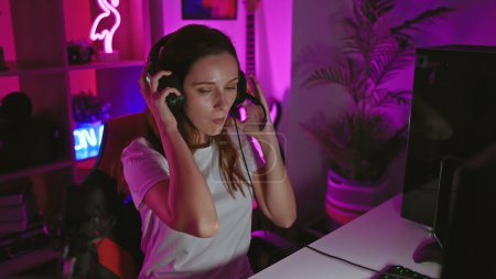 Focused young woman wearing headphones in a neon-lit gaming room at night.