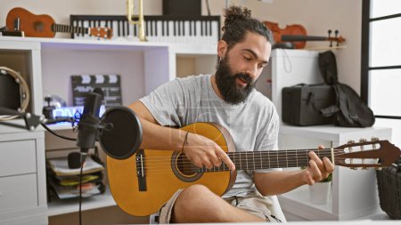 Foto de Hombre hispano tocando la guitarra en un estudio de música casera con micrófono e instrumentos musicales - Imagen libre de derechos