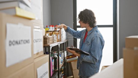 Téléchargez les photos : Young man with clipboard organizing boxes in a light-filled warehouse, wearing a denim jacket. - en image libre de droit