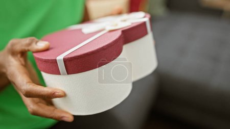 Photo for African woman offering a heart-shaped gift box indoors, signifying love, celebration, or a special occasion. - Royalty Free Image