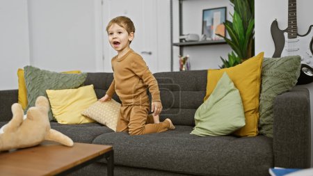 Téléchargez les photos : Un jeune garçon joyeux dans un salon confortable avec un jouet en peluche sur un canapé confortable rempli d'oreillers colorés. - en image libre de droit