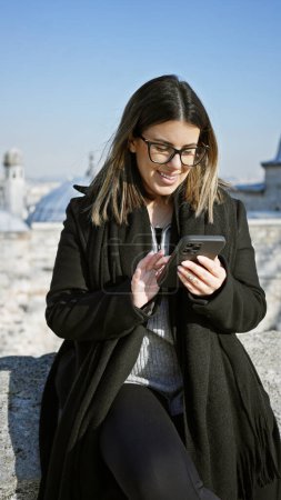 Mujer sonriente usando teléfono inteligente al aire libre en Estambul, resaltado por un fondo de paisaje urbano.