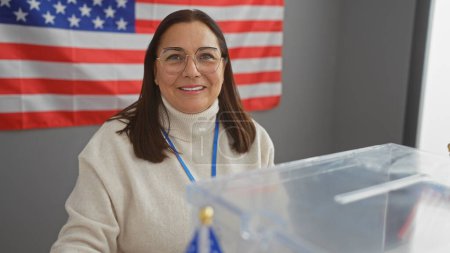 Smiling hispanic woman with glasses at a usa polling station with american flag in the background