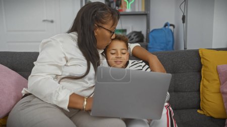 Téléchargez les photos : Une femme embrasse le front de son fils alors qu'ils partagent un ordinateur portable dans un salon confortable, reflétant la famille, l'amour et la technologie. - en image libre de droit