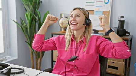 Photo for A joyful caucasian woman celebrates success with headphones in a modern office setting - Royalty Free Image