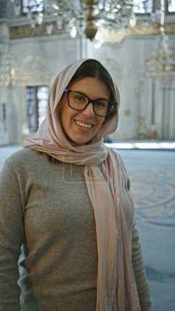 Smiling young woman wearing glasses and hijab inside a historical mosque in istanbul
