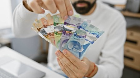 Ein junger bärtiger Mann mit kanadischem Geld in einem Büro, das einen Hauch von Wirtschaft und Finanzen verströmt.