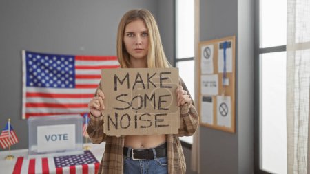 A determined young woman holds a protest sign at a us voting center with flags in background.
