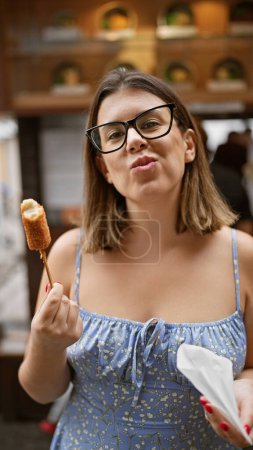 Photo for Hispanic woman in glasses savoring delicious breaded cheese stick on the traditional streets of kyoto - Royalty Free Image