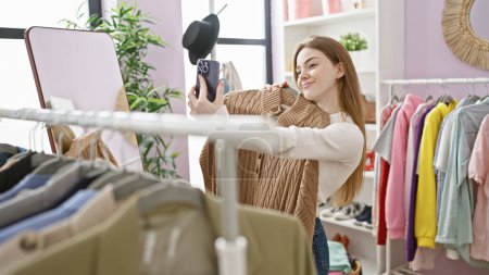 Photo for A young woman takes a selfie in a modern dressing room with various colorful clothes hanging around her. - Royalty Free Image