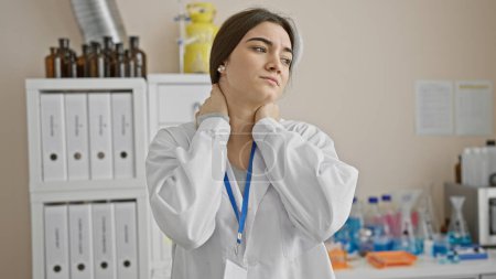 Photo for Hispanic woman with neck pain in lab setting, portraying a medical professional at a clinic. - Royalty Free Image