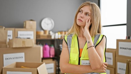 Photo for Pensive young woman volunteer in warehouse with donation boxes contemplating. - Royalty Free Image