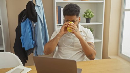 Téléchargez les photos : Un homme afro-américain profite d'une pause café tout en travaillant à la maison, créant une atmosphère détendue et professionnelle. - en image libre de droit