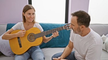 Photo for Father and daughter bonding while sitting on the sofa at home, playing classical guitar; their casual expressions radiate love and relaxed enjoyment in the cozy living room. - Royalty Free Image