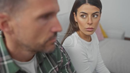 Téléchargez les photos : Un couple hispanique apparaît contemplatif dans leur salon, la femme regardant anxieuse aux côtés de son homme sur le canapé. - en image libre de droit