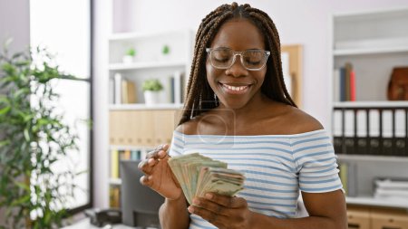 Smiling african woman with braids counting uae dirham banknotes in a modern office setting
