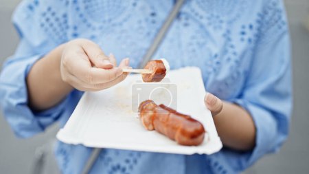 Photo for Beautiful hispanic woman eating Ksekrainer sausage in the streets of Vienna - Royalty Free Image