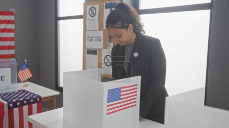 Hispanische Frau wählt in einem amerikanischen Wahlzentrum, das mit Fahnen geschmückt ist.