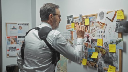 A mature man analyzes a crime evidence board in a detective's office, surrounded by photos, notes, and fingerprints.