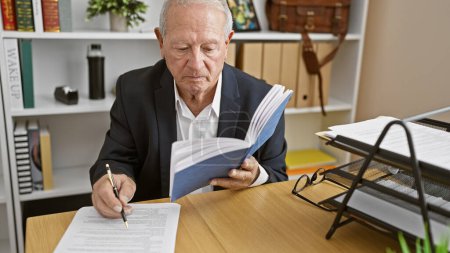 Foto de Hombre mayor enfocado en el trabajo, leyendo con confianza un libro y tomando notas, inmerso en un papeleo serio de negocios en la oficina. - Imagen libre de derechos